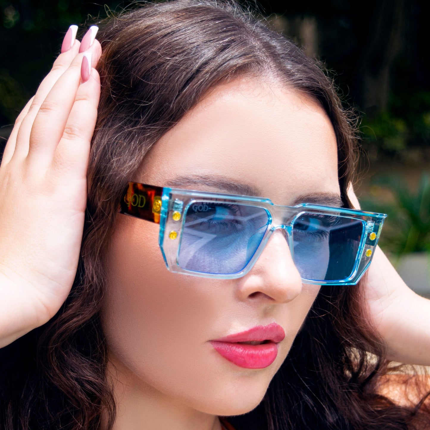 Woman wearing Island God blue flat-top sunglasses with gold stud details and tortoiseshell arms, showcasing bold Caribbean streetwear style.